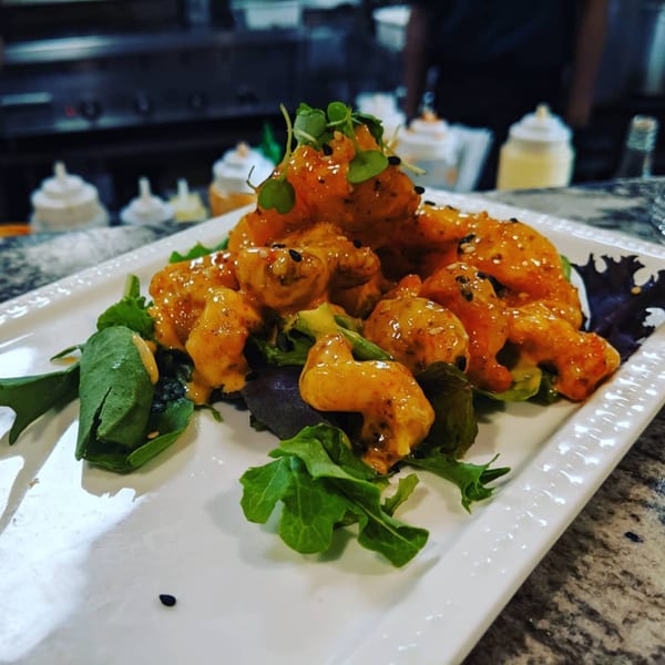 Itto Ramen's Bang Bang Shrimp, coated in orange sauce, served on a bed of mixed greens.