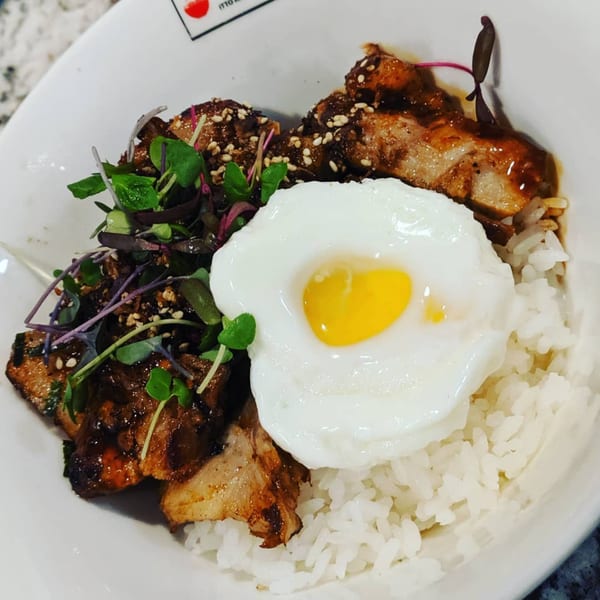 Itto Ramen Bar's rice bowl with grilled pork, a fried egg, sesame seeds, and microgreens.