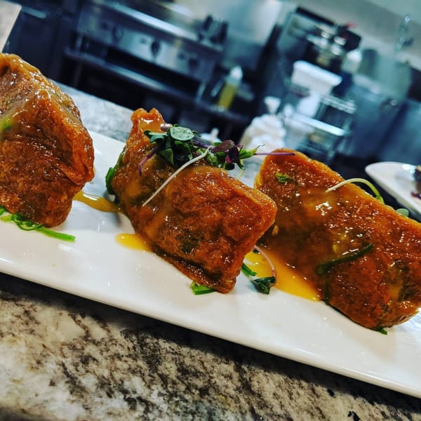 Three glazed Itto Ramen Bar & Japanese Tapas appetizers on a white plate with a kitchen in the background.