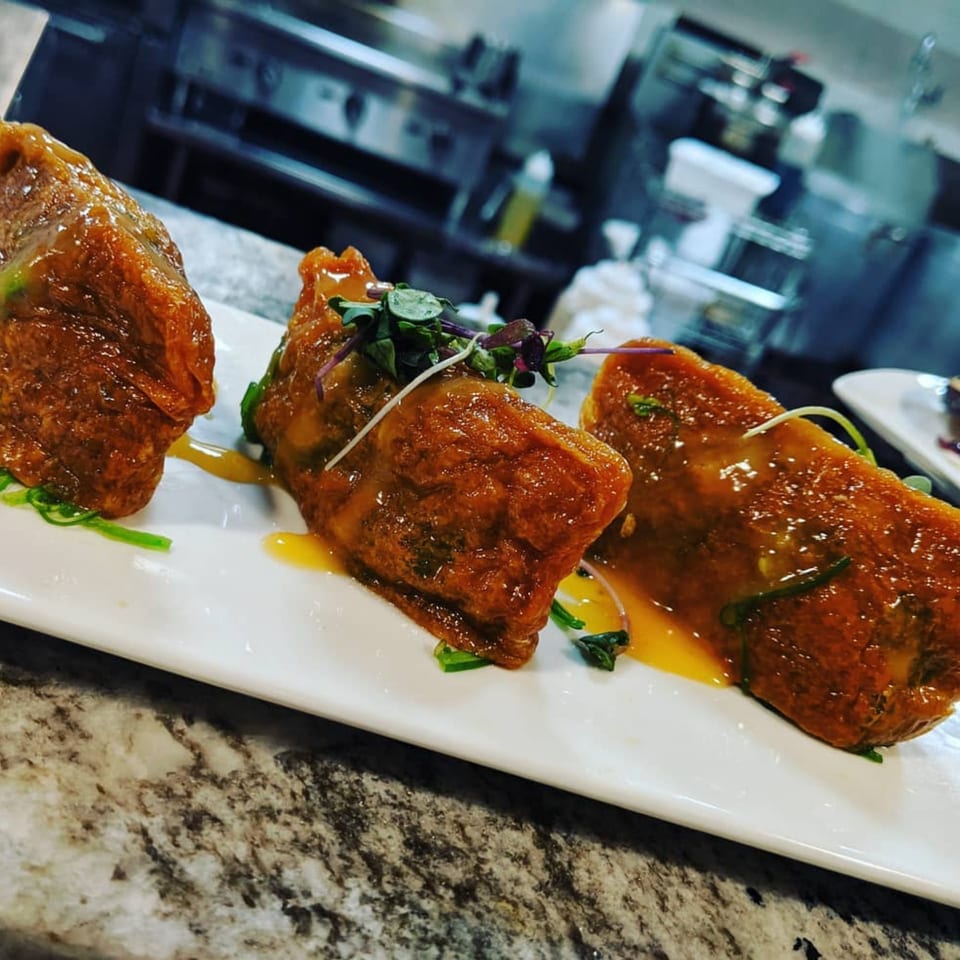 Three glazed Itto Ramen Bar & Japanese Tapas appetizers on a white plate with a kitchen in the background.