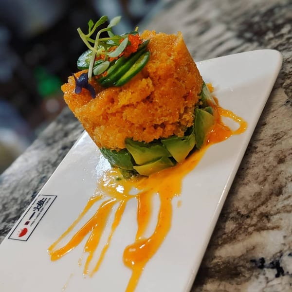 Itto Ramen Bar's spicy salmon avocado tower, garnished with microgreens and orange sauce.