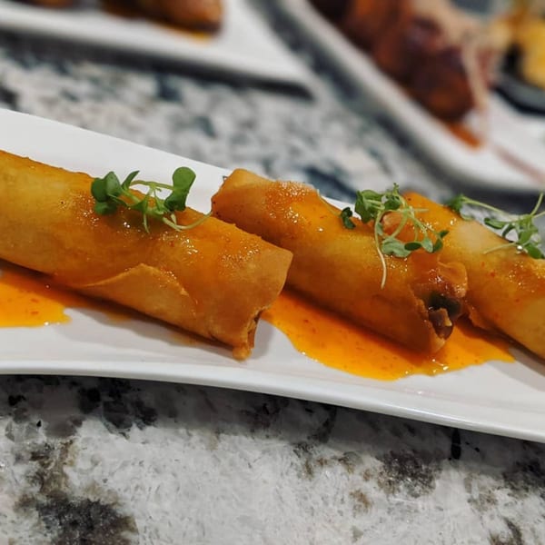 Crispy Itto Ramen spring rolls drizzled with orange sauce and garnished with microgreens on a white plate.